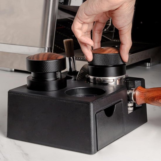 Hand draait aan houten tamper bovenop zwarte barista tamper station.