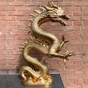 Gouden draak ornament voor een bakstenen muur, staand op een donkere sokkel.