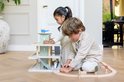 Twee kinderen spelen met een pastelgroene houten speelgoedgarage en een houten treinbaan op een parketvloer.