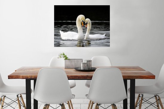Deux cygnes blancs au bec orange nagent dans l'eau sombre, leurs cous forment un cœur, accrochés au mur au-dessus d'une table.