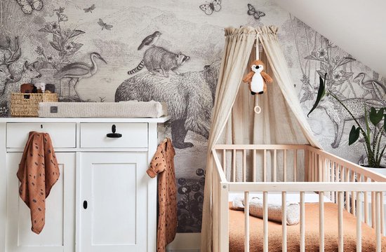 Kinderkamer met dierenbehang, wiegje en commode met bruine doeken.