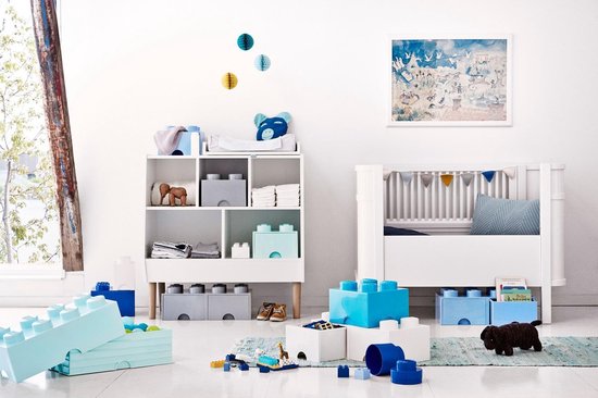 Chambre d'enfant avec des étagères blanches, des boîtes de rangement LEGO, un berceau et des jouets, y compris de grandes briques LEGO bleu clair.