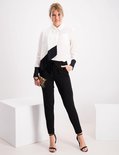 Model in een zwart-wit shirt en zwarte broek met strikceintuur, hoge hakken en luipaardprint tasje.