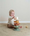 Een baby met een gebreide vest speelt met een spiraaltoren in zachte pasteltinten.