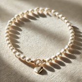 Crèmekleurige parelketting met gouden hartvormige bedel op een textuur achtergrond.