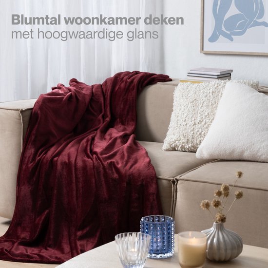 Bordeauxrode woondeken over een beige bank in een woonkamer. Glanzende afwerking.
