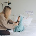Mère avec bébé dans une cape de bain bleue sur un lit, "Super doux grâce au coton 100% à tissage court" en texte.