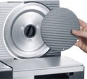 Een hand houdt een grijze geribbelde schijf tegen een metalen snijmachineblad.