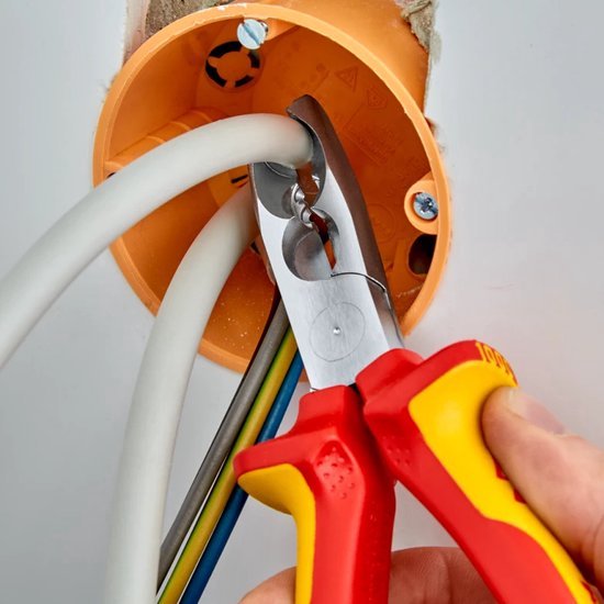 Hand gebruikt rode en gele tang om dikke witte kabel te snijden in een oranje elektriciteitsdoos.
