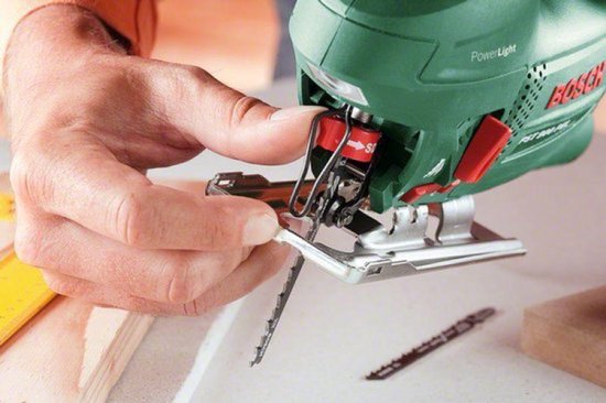 Hand vervangt zaagblad van groene Bosch decoupeerzaag.