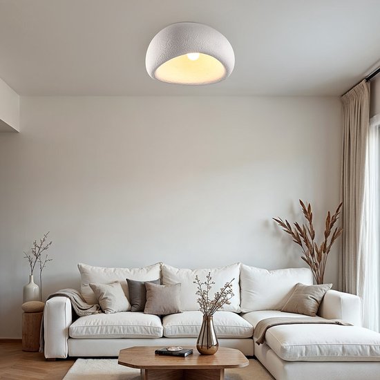 Wit plafondlamp met steeneffect, bolvormig met een opening aan de voorkant. Staat boven een witte bank.