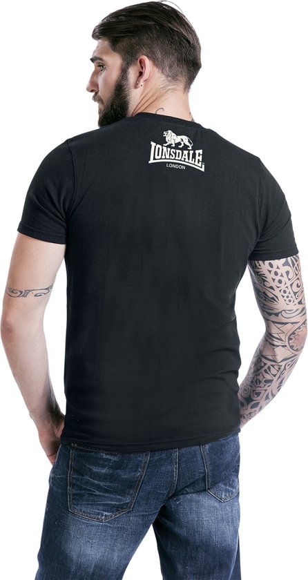 Man met baard en tatoeages, van achteren gezien, draagt een zwart Lonsdale London T-shirt.