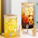 Twee glazen drankdispensers met houten standaard en kraantje, gevuld met schijfjes fruit en ijs.