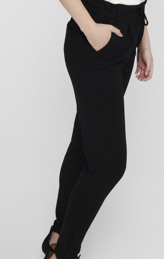 Zwarte broek met ceintuur, zijzakken en een cropped pasvorm, gedragen met hoge hakken.