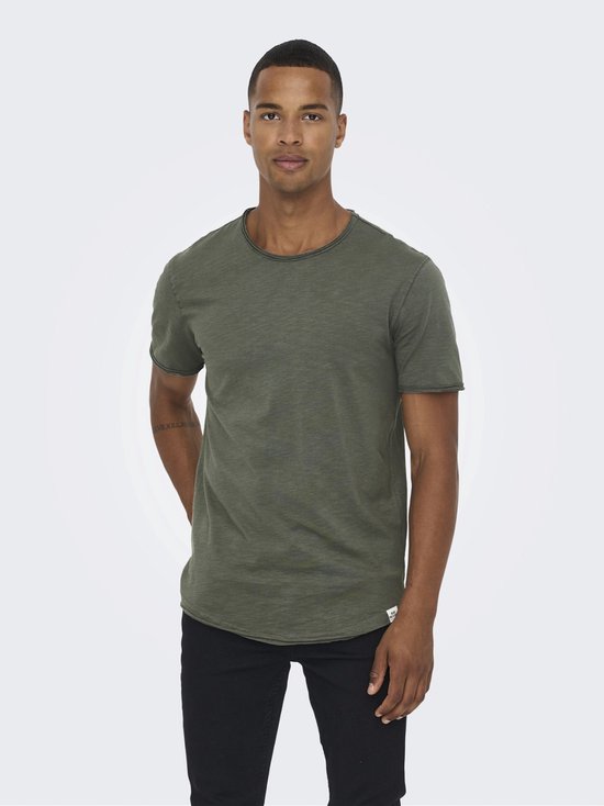 Man in olijfgroen T-shirt met een licht verouderde afwerking en zwarte jeans.