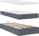 Drie onderdelen van een bed: een witte topper, een donkergrijs matras, en een bedombouw met lattenbodem.