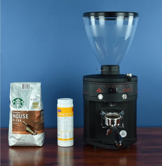 Een zak Starbucks koffiebonen, een pot Urnex Grindz GO reiniger en een zwarte Peak koffiemolen.