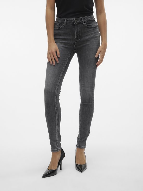 Model draagt een grijze skinny jeans met middelhoge taille en zwarte puntige pumps.