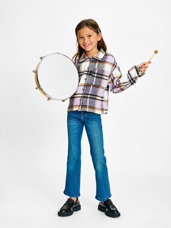 Meisje met drum, draagt jeans en een geruite blouse in paars en bruin.
