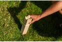 Een hand plaatst een houten pion met een kroonvormige top in het gras.