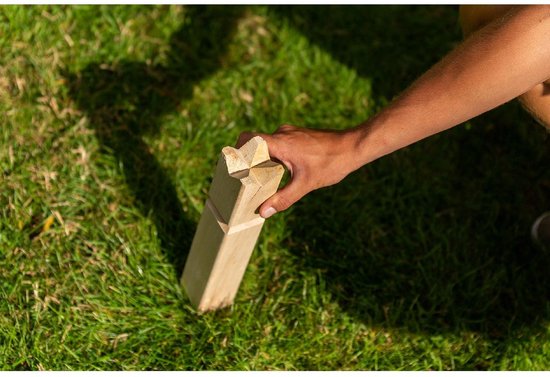 Een hand plaatst een houten pion met een kroonvormige top in het gras.
