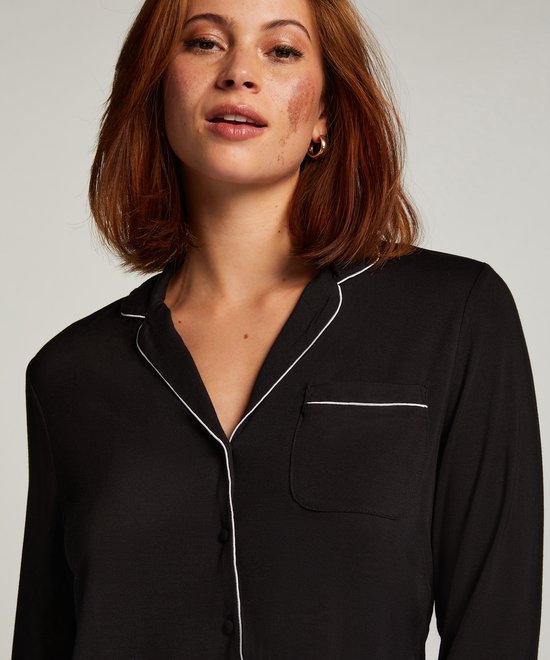 Model met rood haar en sproeten draagt een zwart pyjamashirt met witte biezen en opgestikte borstzak.