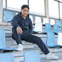 Jongeman in donkerblauw trainingspak, zittend op een tribune.