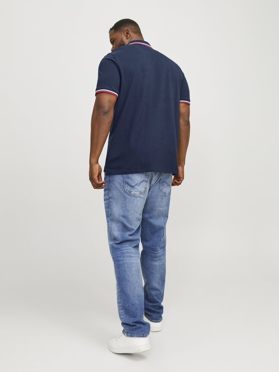 Man in donkerblauwe polo met rode en witte strepen, kijkt naar beneden.