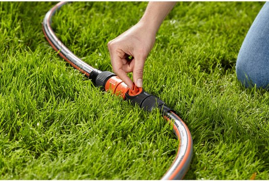 Een hand met oranje en zwarte tuinslangkoppeling met hendel, in groen gras.