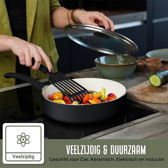 Vrouw in groene blazer bakt groenten in een witte koekenpan met zwarte handgreep op een kookplaat.