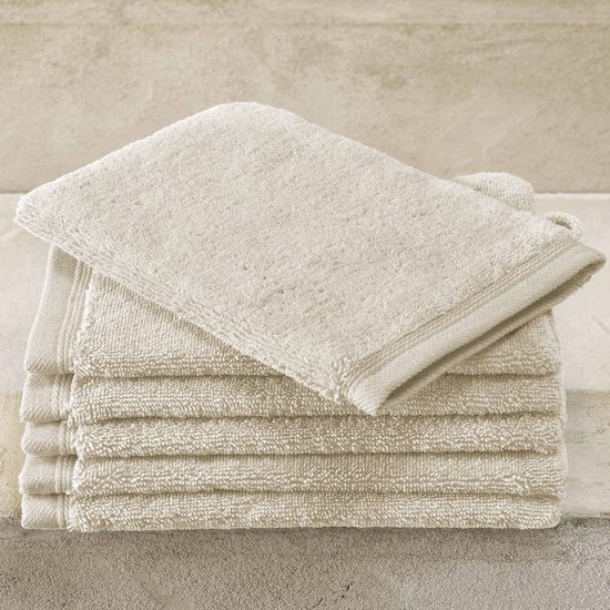 Pile de gants de toilette beiges avec une boucle, sur une surface en béton.