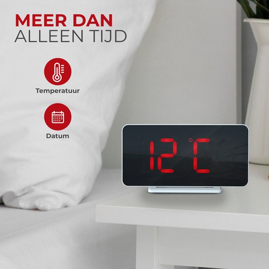 Witte digitale wekker met rood display dat 12 graden Celsius toont. Naast de wekker liggen een bril, een plant en een mok.