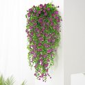 Hangende plant met veel kleine roze bloemen en groene bladeren, tegen een witte muur.