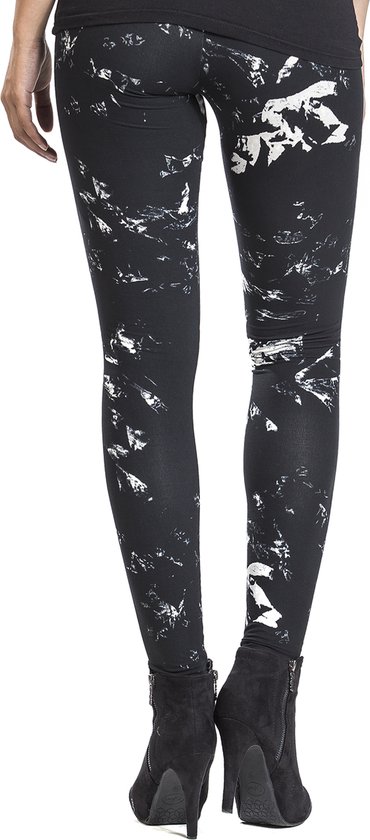 Zicht op de achterkant van een vrouw in zwarte legging met witte spettersprint, staand in enkellaarsjes.