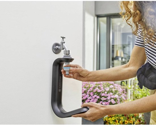 Een vrouw met gestreepte trui bevestigt een Gardena kraanaansluitstuk aan de Gardena Liano TapFix slanghouder, gemonteerd aan een witte muur.