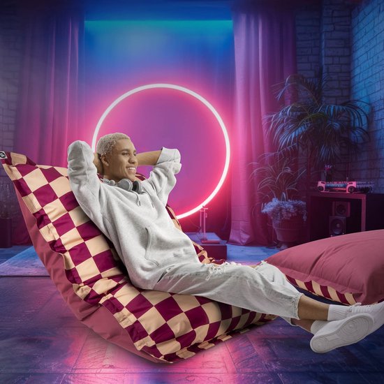 Vrouw met blonde kuif en tattoo's op een paars-crèmekleurige dambord zitzak in een neonverlichte kamer.