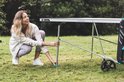 Vrouw met lichte kleding, knielend bij een grijze tafeltennistafel.