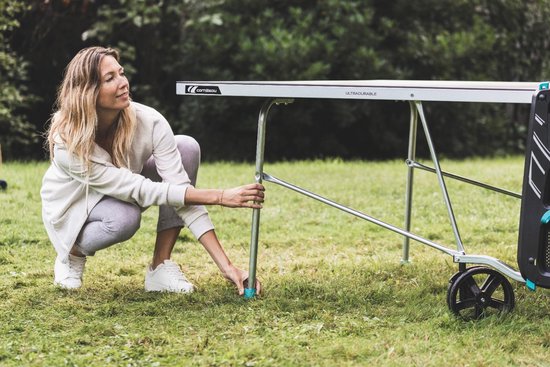 Vrouw met lichte kleding, knielend bij een grijze tafeltennistafel.