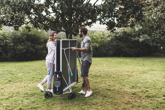 Man en vrouw in een tuin bij een grijze tafeltennistafel die ze verplaatsen
