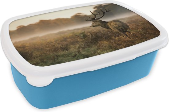 Lunchbox bleue avec un couvercle blanc orné d'un cerf dans un paysage automnal brumeux.