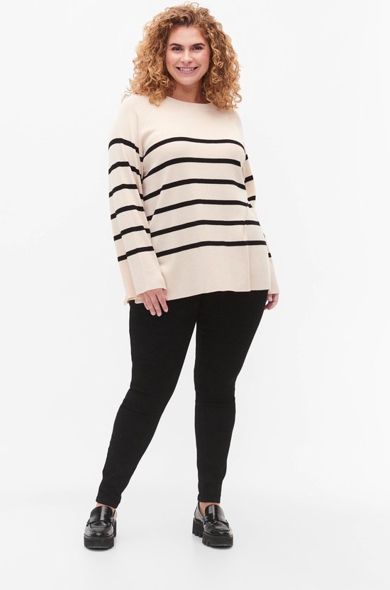 Model met blonde krullen draagt een gebreide trui met horizontale zwart-witte strepen en zwarte skinny jeans.