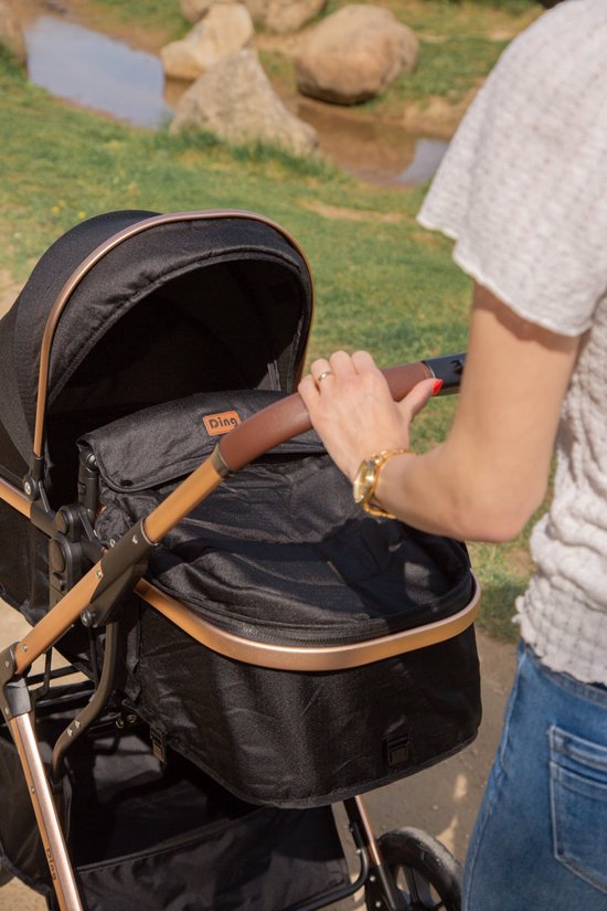 Zwarte kinderwagen met goudkleurige accenten, terwijl een vrouw de duwbeugel vasthoudt.