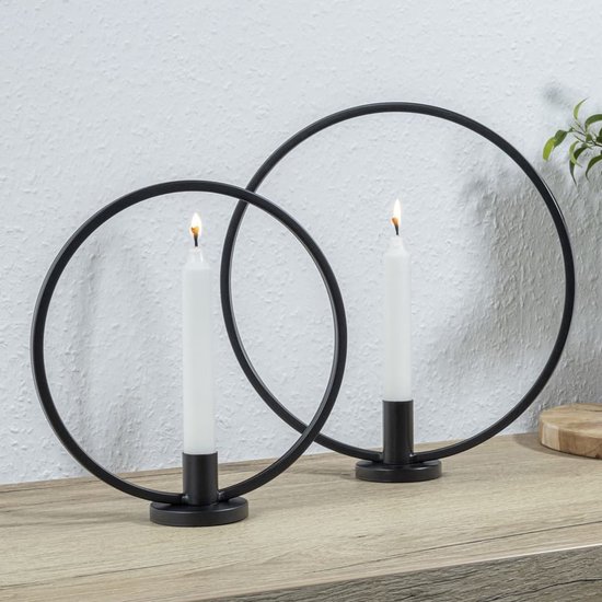 Twee zwarte ringkandelaren met witte kaarsen, op een houten plank.