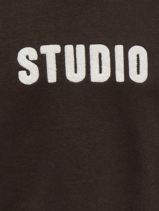 Detail van witte 'STUDIO' letters op een bruine sweater.