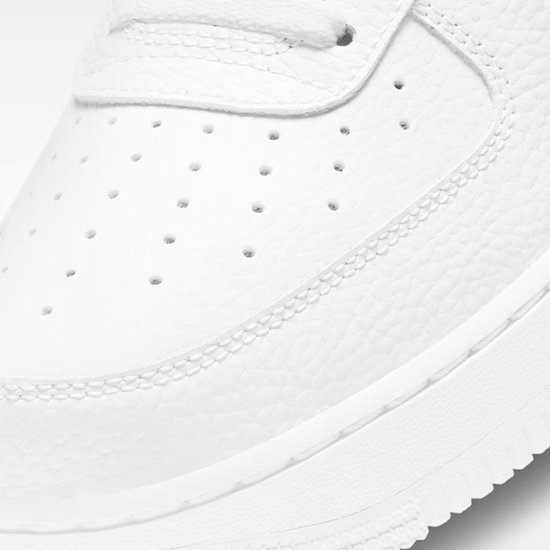 Witte sneaker van generfd leer, close-up van de neus met perforaties en stiksels.