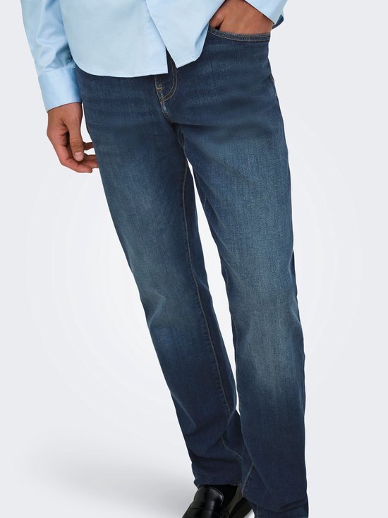 Close-up van een man in een lichtblauwe blouse en donkere jeans met lichte slijtage op de dijen.
