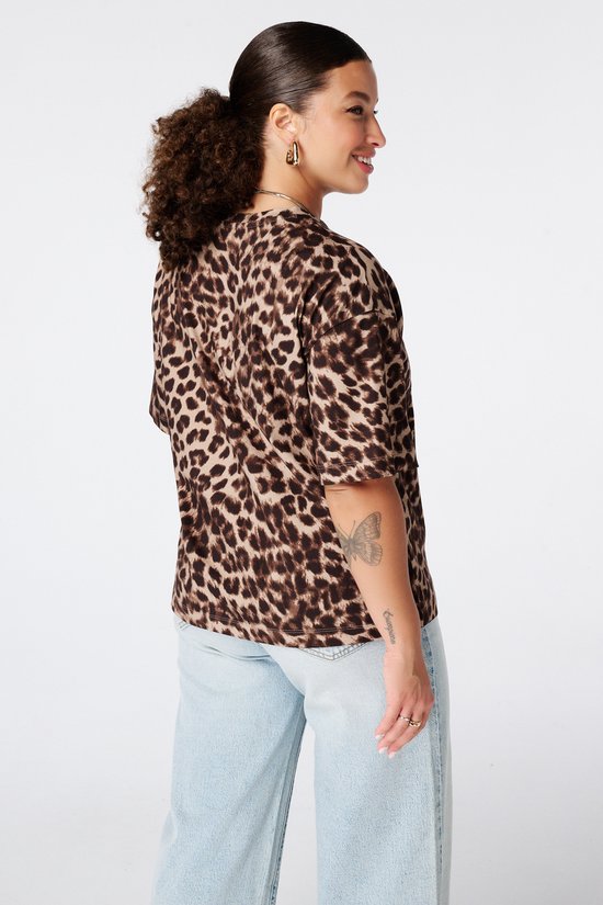Model draagt een bruin t-shirt met dierenprint, van opzij gezien.