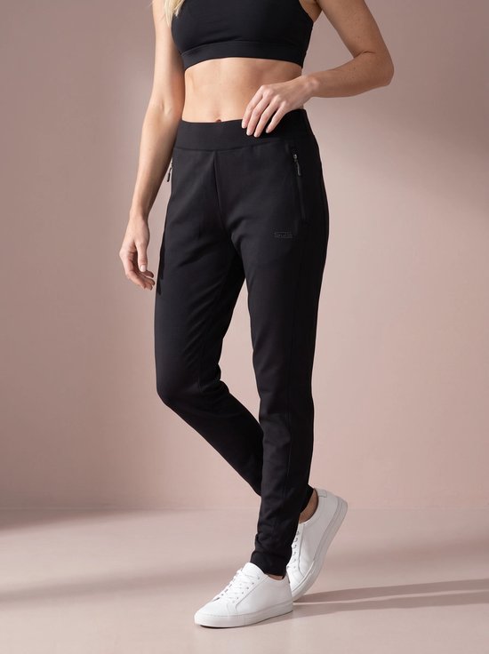 Vrouw in zwarte sportbroek met ritszak en logo "SDS", met witte sneakers.