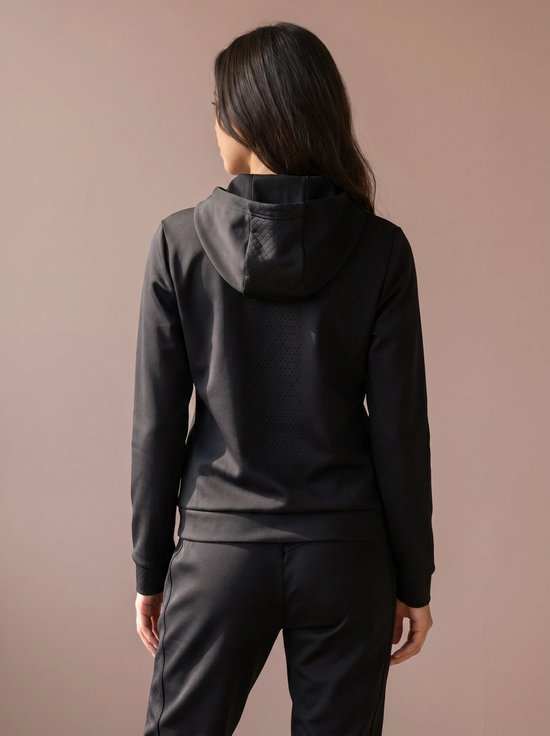 Achterkant van een model met een zwarte hoodie met rits en een zwarte broek. De hoodie heeft een ruitpatroon op de capuchon en geperforeerd materiaal op de rug.