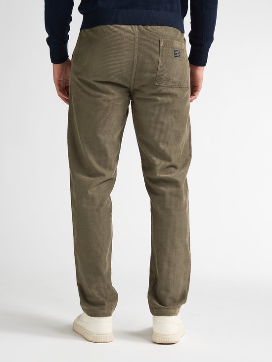 Model draagt een olijfgroene corduroy broek en marineblauwe trui, achteraanzicht.